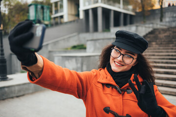 Young woman wearing a coat and hat takes a photo of herself