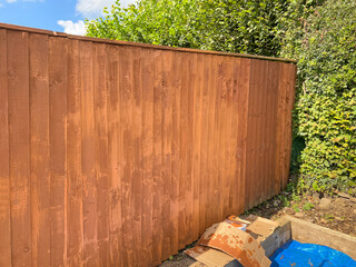 Wooden fence panels being painted with wood rpeserver. The lighter patches are where new paint is drying. No people. Copy space.