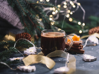 A glass Cup of hot espresso coffee on the table, a garland in the form of a Christmas tree, branches, warm winter knitted things and cinnamon sticks. Homely atmosphere and comfort