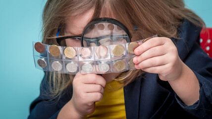 Child numismatist. Kid with a magnifying glass is considering the old coin numismatist. Financial education. Back to school.
