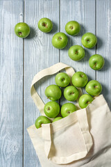 Cloth bag with green apples on a wooden background.