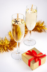 Two glasses with champagne, gold gift box and Christmas decoration with snowflakes on white background