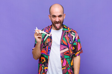 young bald man with cheerful, carefree, rebellious attitude, joking and sticking tongue out, having...