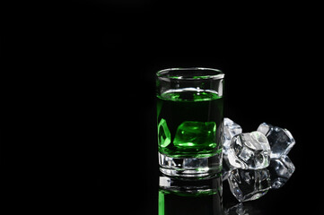 Absinthe shot with ice cube on black background