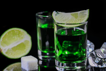 Absinthe shots with lime slices and sugar on black background