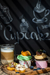 Cupcakes with fruits and berries and coffee on a wooden table, a wall with chalk drawings, different light effects.
