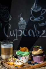Cupcakes with fruits and berries and coffee on a wooden table, a wall with chalk drawings, different light effects.