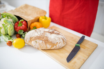 Bread on cutting board next to a bag of vegetables