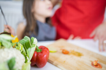 Little girl and her father slicing vegetables on a cutting board