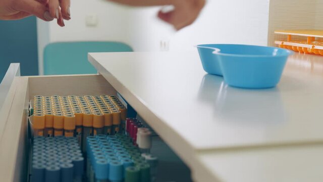 storage of blood test tubes. The lab technician opens the drawer for storing test tubes and takes out various medical devices and test tubes.