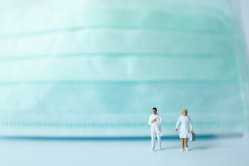 Healthcare Concept. Closeup of docter and nurse miniature figure people walking with surgical face mark as background.