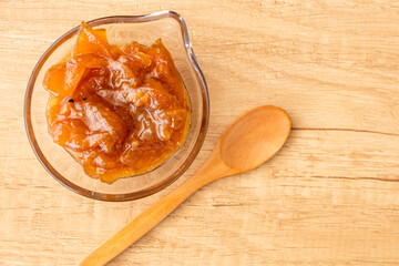 Glass pot with a delicious homemade apple and onion chutney, with cinnamon on a light wooden board....