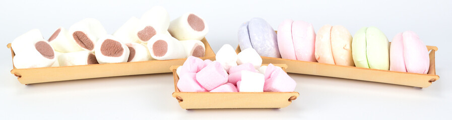 Variety of marshmallows laid out on wooden trays on a white background