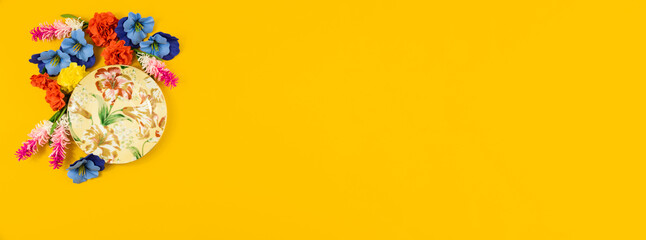 Cozy home concept, saucer and flowers on a plain yellow isolated background, top view, flat lay banner