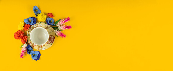 Yellow background and saucer for an empty cup of tea surrounded by flowers, copy space, flat lay,...
