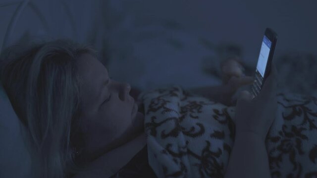 A fat woman lies in bed and checks her smart phoneat night.