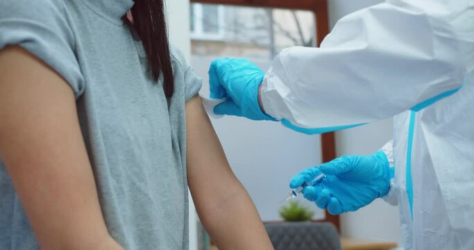 Close up of professional healthcare worker in protective uniform and gloves making injection to young female patient in hospital cabinet. Analysis. Vaccination concept. Coronavirus pandemic covid-19