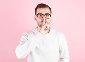 Young handsome man over pink background asking to be quiet with finger on lips. Silence and secret concept.