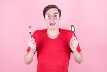 Hungry man holds a fork and spoon in his hands and thinks about delicious food over pink background . Diet and meal concept.