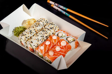 Sushi Sets Uramaki, California, Philadelphia, on a white plate. Festive, New Year concept. Against a dark reflective background.