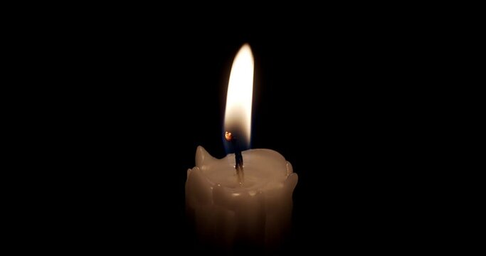 A single white candle burning.Isolated candle burning with dark background.White paraffin candle with yellow shades burns on a black background.Background or illustration of remembrance or celebration