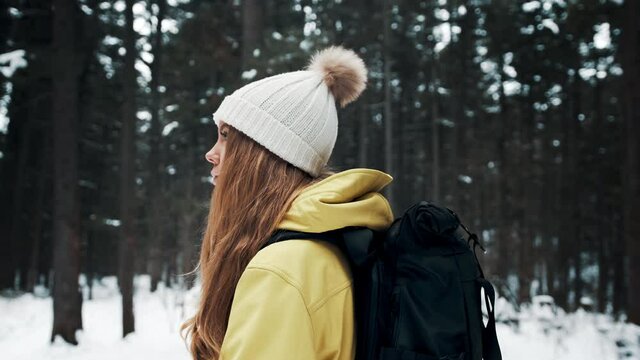 Girl with a white hat in the forest with a backpack in winter. Side view
