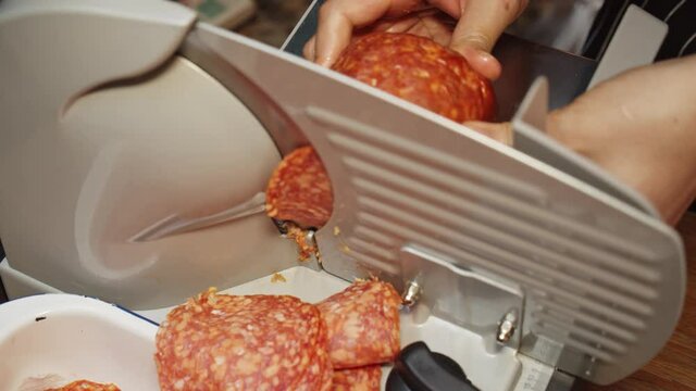 Chef slices salami on meat slicer machine. Outdoor  event catering.