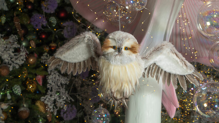 Christmas toy in the form of owl. Decorated christmas tree background. Happy new year concept. Blurred background with lights.