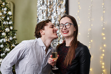 Woman,dressed up in fancy black dress with champagne glass, laughing and man in white shirt, biting her earring at New Year party celebration. Male and female differences.Stay home for winter holidays