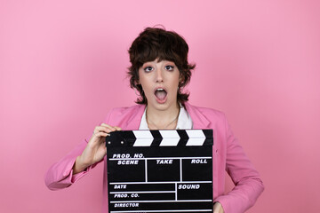 Young business woman over isolated pink background holding clapperboard very happy having fun