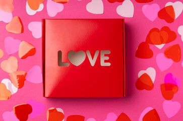 Red box with word Love in heart shaped with a lot of confetti in heart shaped on rose background