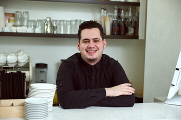 An arms crossed handsome man smiling at the camera behind the bar
