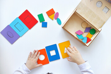 Learning colors and shapes. Children's wooden toy. The child collects a sorter. Educational logic toys for kid's. Children's hands close-up. Montessori Games for Child Development.