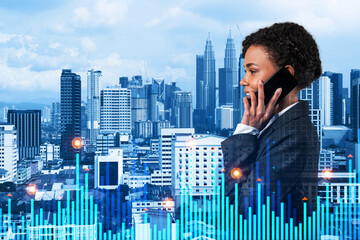 Attractive black businesswoman pensively processing conference call by phone to find financial solution for venture capital project. Hologram chart over Kuala Lumpur city background
