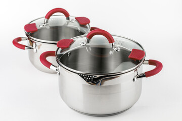 Stainless casserole with glass lid and red handles on grey background.