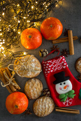 Christmas stocking, cinnamon sticks, tangerines and cookies on dark gray background with copy space. Festive decorations top view photo. 
