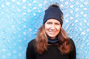 Beautiful middle-aged woman in a warm winter hat and scarf on a light blue background, a woman smiling and happy because she will not be cold in winter. The concept of health