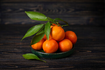 Sweet juicy orange New Year's clementine tangerines, mandarines with green leaves. Citrus still life on a brown wooden background. Healthy winter fruits with vitamin C to boost immunity.