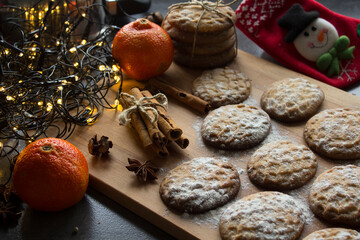 Christmas biscuits with festive decoration. Top view photo of homemade cookies, Christmas lights, tangerines, star anise and cinnamon sticks. 
