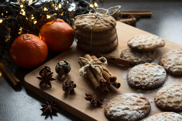 Christmas biscuits with festive decoration. Top view photo of homemade cookies, Christmas lights, tangerines, star anise and cinnamon sticks. 
