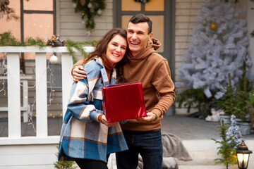 Couple hugging and celebrating New year outdoors. They holding red box with Valentine's gift. They laughing and enjoying