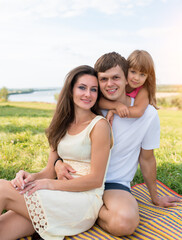 happy family, woman mom with man dad, girl daughter 5-6 years old, fun joyful outdoor picnic, parenting, emotions of happiness, delight, fun and joy. Summer in park sitting blanket, stylish clothes.