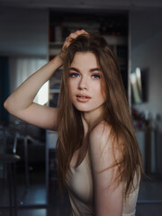 Fototapeta premium Fashion photo of beautiful young beautiful woman with gorgeous natural lips wearing shoulder straps blouse relaxing and smiling in dark room staring into camera