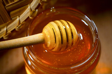 Liquid honey with a honey dipper in a glass jar on a wooden table. Healthy organic honey. Close-up,...