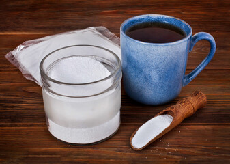 Fructose in a transparent pack with cup of tea, jar and scoop of sorbitol on a wooden background. Different sweeteners concept.