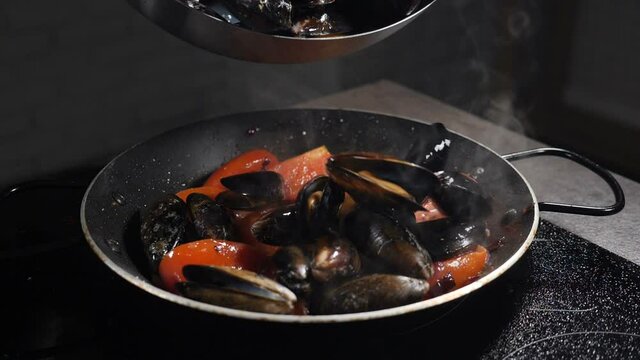 Chef pouring mussels into frying pan toassing and stirring. Slow motion food video. Process of cooking Italian pasta with mussels in tomato sauce. Traditional Mediterranean cuisine. Full hd