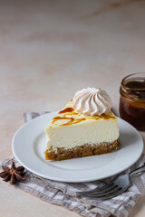 Piece of carrot vanilla cheesecake with salted caramel topping and meringue on a white ceramic plate, light concrete background.