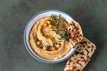Classic hummus with rosemary, flatbread, boiled chickpea and olive oil, green stone background. Traditional Middle Eastern snack. Top view.