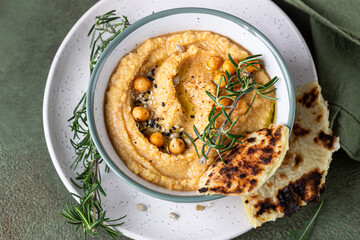 Classic hummus with rosemary, flatbread, boiled chickpea and olive oil, green stone background. Traditional Middle Eastern snack. Top view.