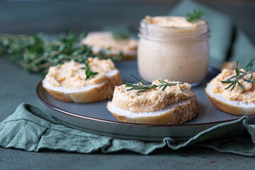 Sandwiches with smoked salmon and soft cream cheese pate or mousse with thyme and rosemary on a ceramic plate, green concrete background.